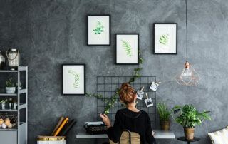 Woman sitting at desk in loft style apartment with grey walls and prints of plants on the wall