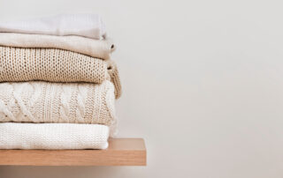 A stack of sweaters folded on a shelf in the closet